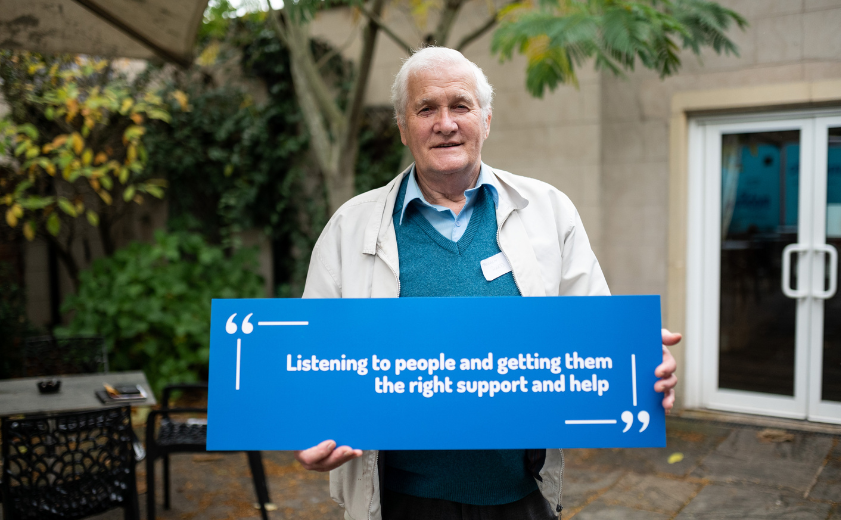 Man holding sign which says: "listening to people and getting them the right support and help"